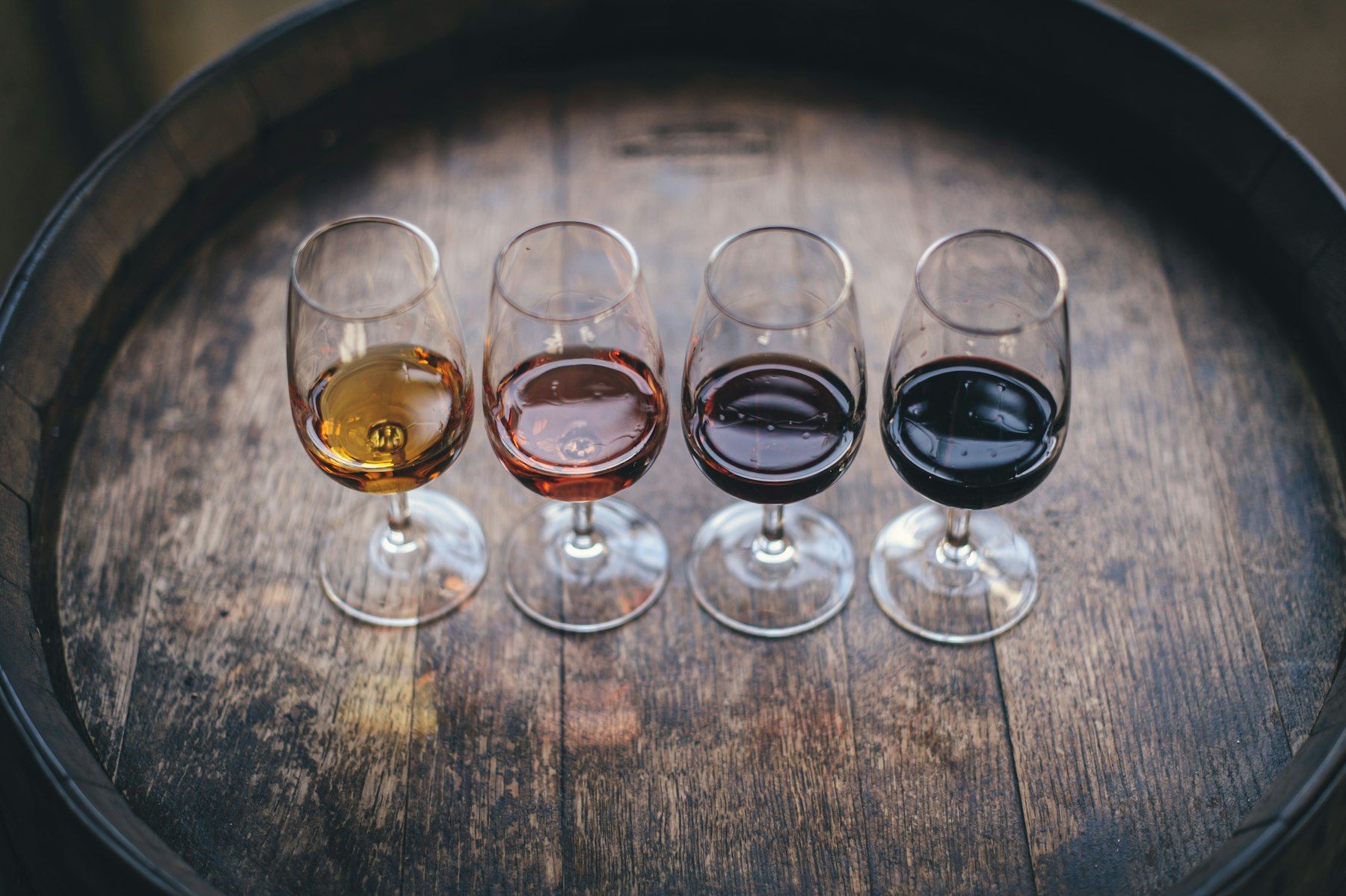 Vier Probiergläser mit Weiß-, Rosé- und Rotwein auf einem Holzfass