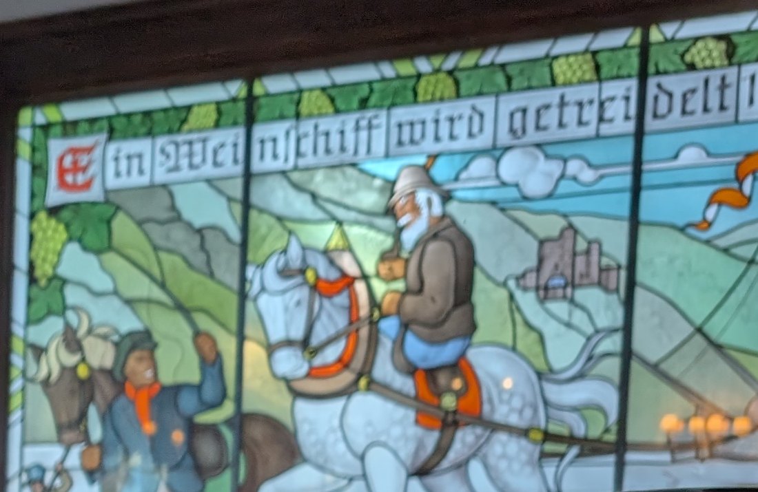 Bleiglasfenster mit der Inschrift „Ein Weinschiff wird getreidelt“: ein Treidler auf einem Schimmel zieht ein Schiff am Ufer entlang