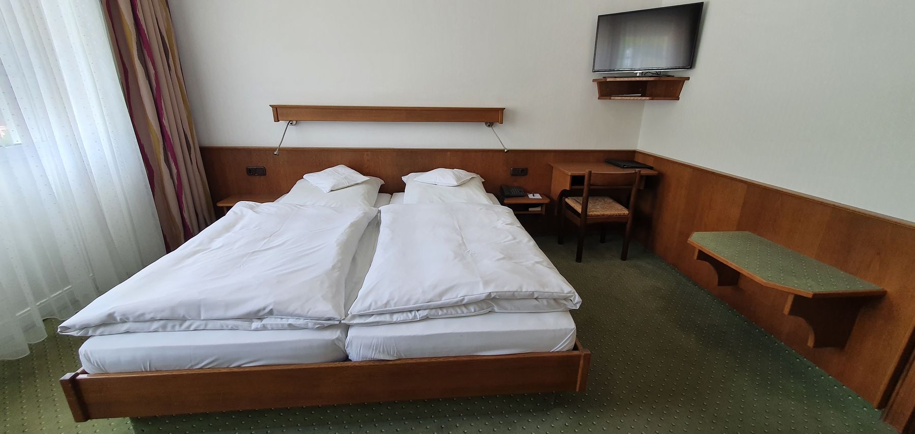 Doppelbett mit Holzkopfteil, Ablage und Fernseher an der Wand