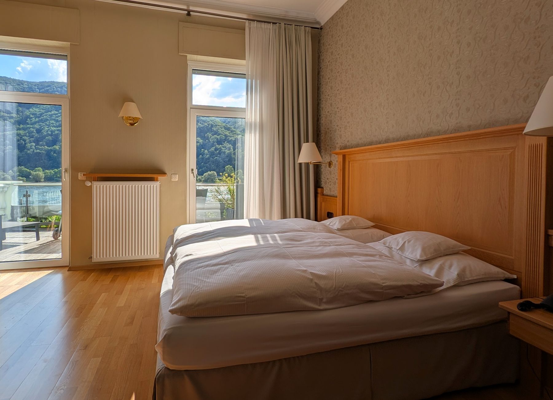 Frisch bezogenes Doppelbett auf warmem Parkett, daneben Fenster und Balkontür