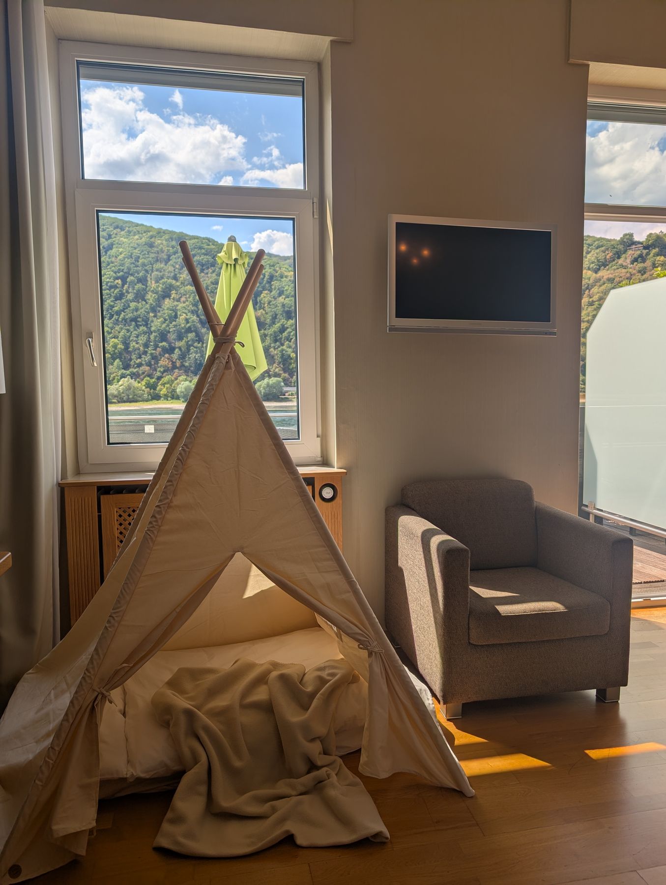Sessel und Spielzelt am hohen Fenster, draußen der bewaldete Hang über dem Rhein
