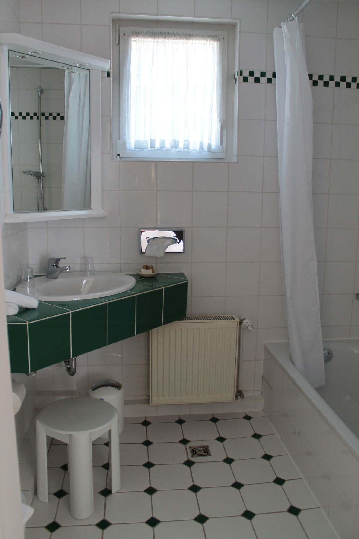 Bad der Junior Suite mit Badewanne, grün gefliestem Waschtisch und Fenster