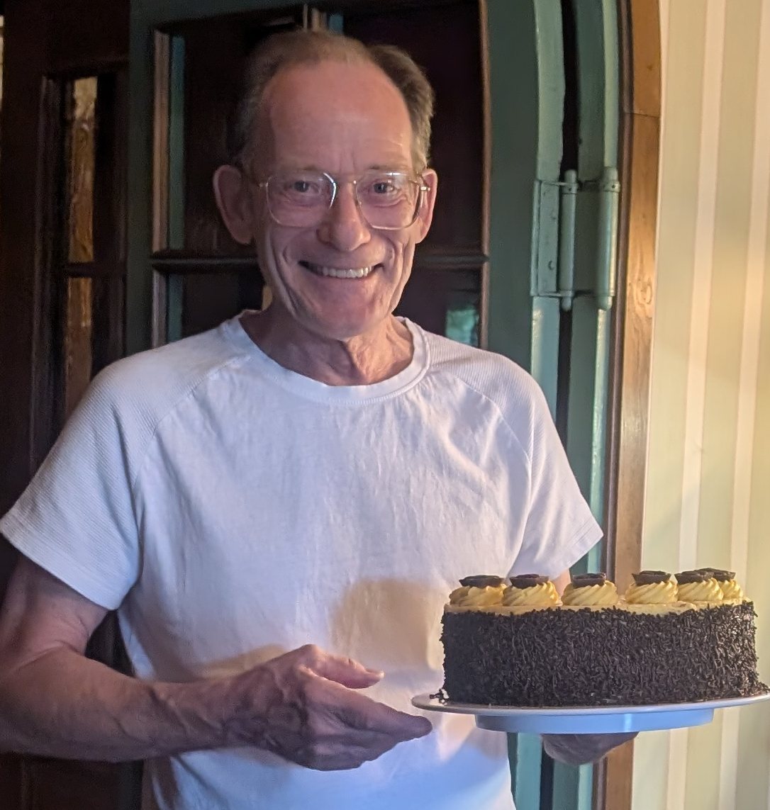 Hans Kellner hält lächelnd eine frisch gebackene Torte mit Schokoladenstreuseln
