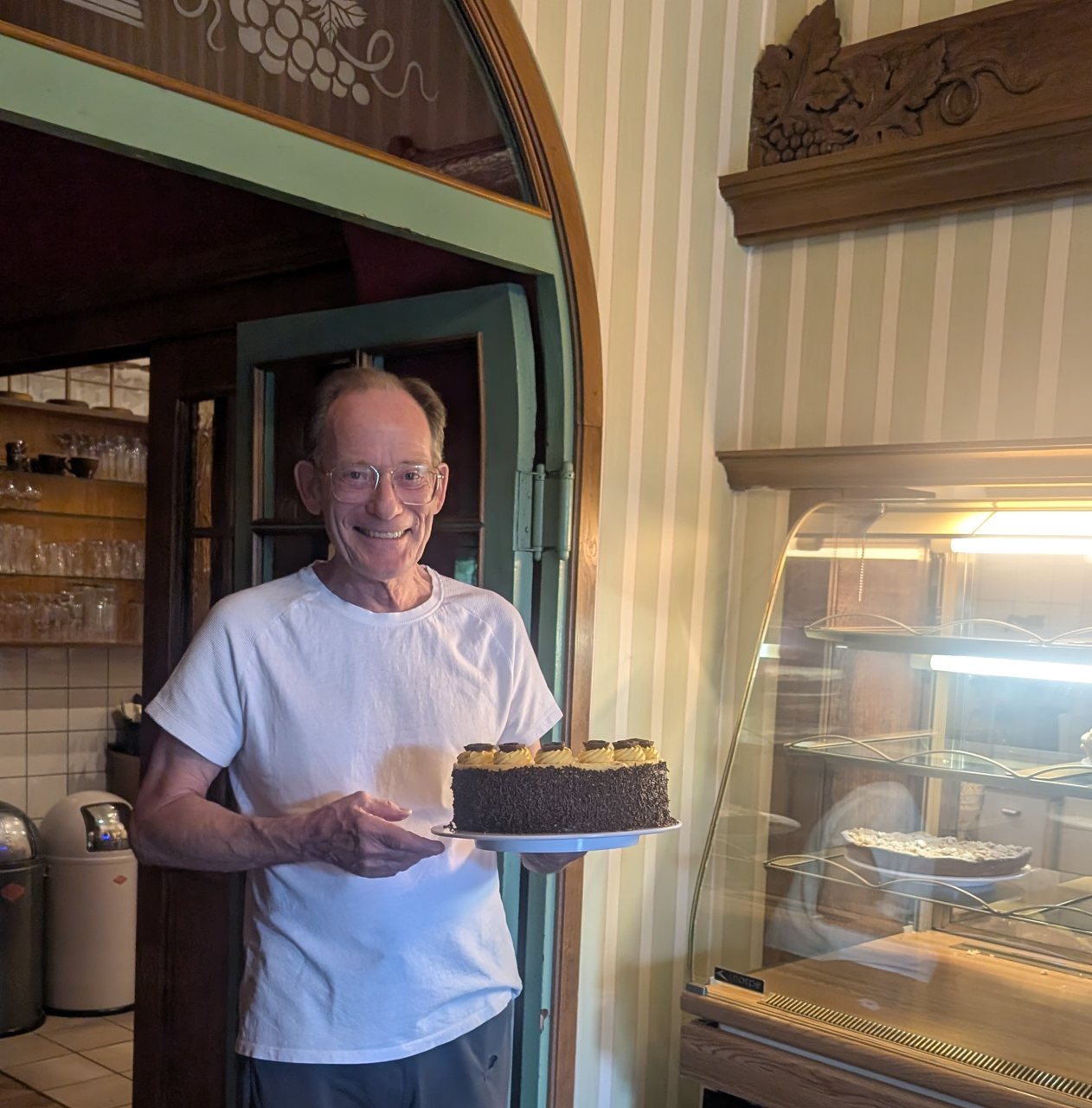 Konditor Hans Kellner mit einer Schokoladentorte neben der Kuchenvitrine